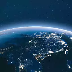 View of Earth from space at night showing illuminated cities across Asia, with a star-filled sky in the background.