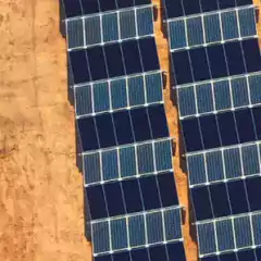 Aerial view of solar panels installed on a sandy ground, arranged in parallel rows for efficient sunlight capture.