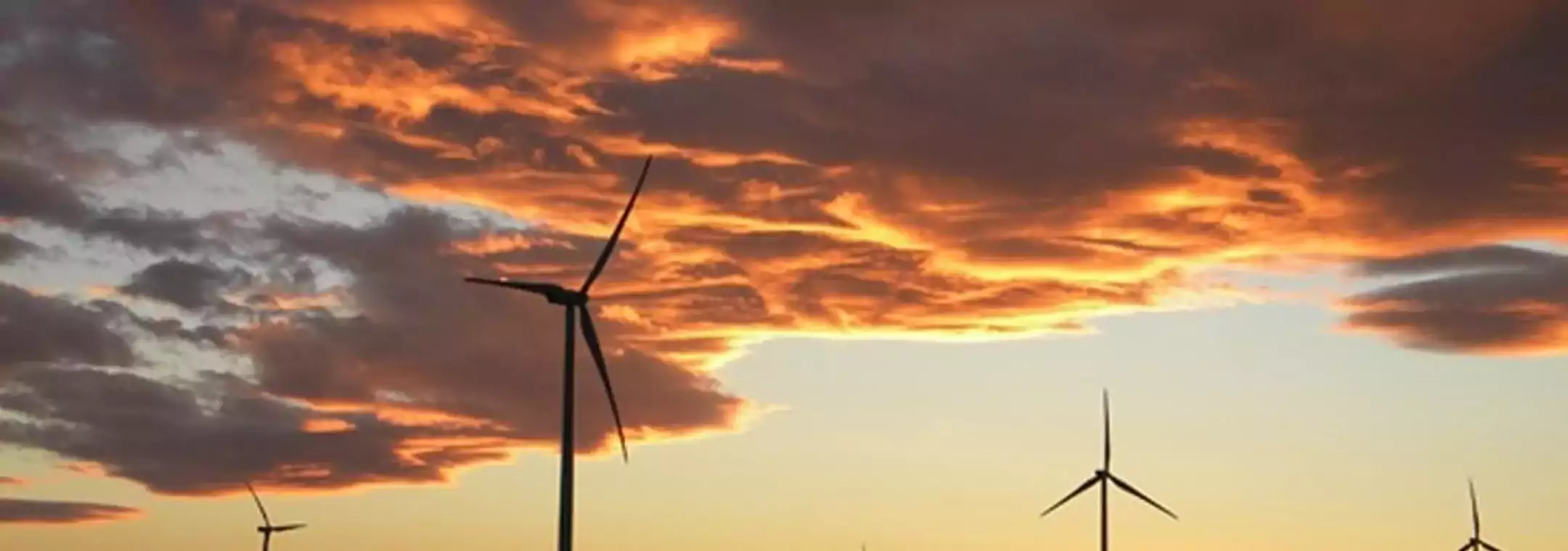 Wind turbines silhouetted against a dramatic sunset sky with orange and purple clouds, illustrating renewable energy in a natural landscape.
