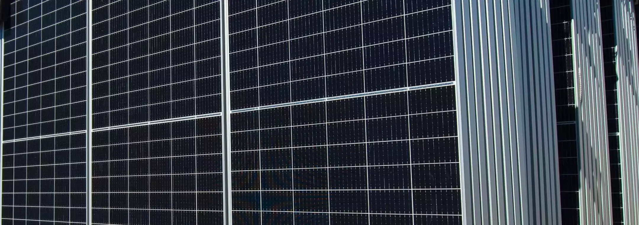 Stack of large solar panels arranged vertically on a concrete base outdoors, with a clear blue sky in the background.