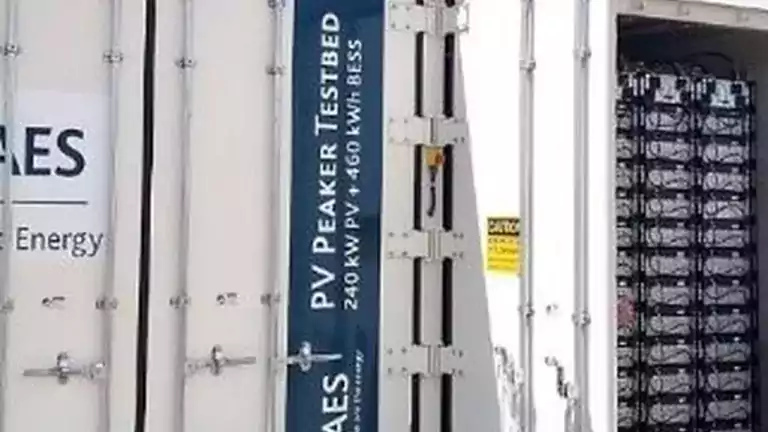 A close-up of a white container labeled 'PV Peaker Testbed 240 kW PV + 460 kWh BESS' with visible battery storage units inside, used for solar energy storage and testing.