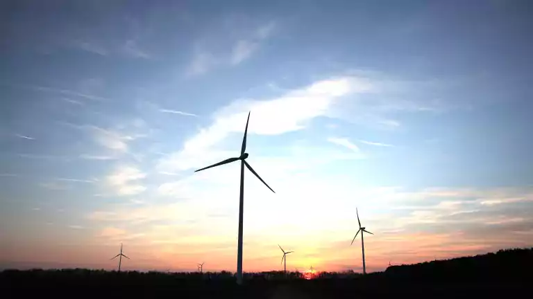 Silhouettes of wind turbines on an open field at sunset with a colorful sky and scattered clouds.