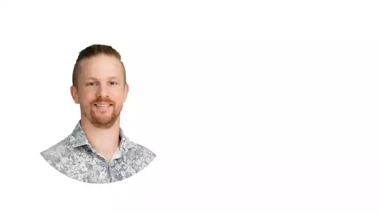 Smiling man with short light brown hair and beard wearing a patterned shirt, shown in a circular portrait on a white background.