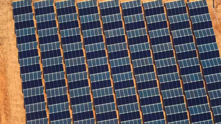 Aerial view of rows of solar panels installed on a dry, sandy field, capturing sunlight for renewable energy production.