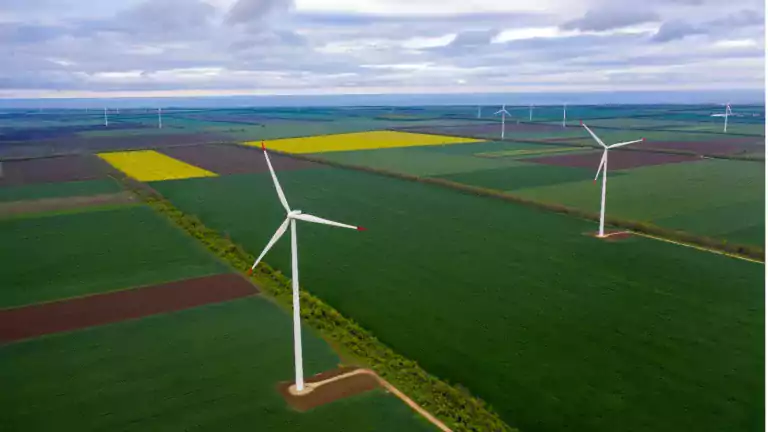 Aerial view of wind turbines on green and yellow agricultural fields under a cloudy sky, illustrating renewable energy and sustainable farming.