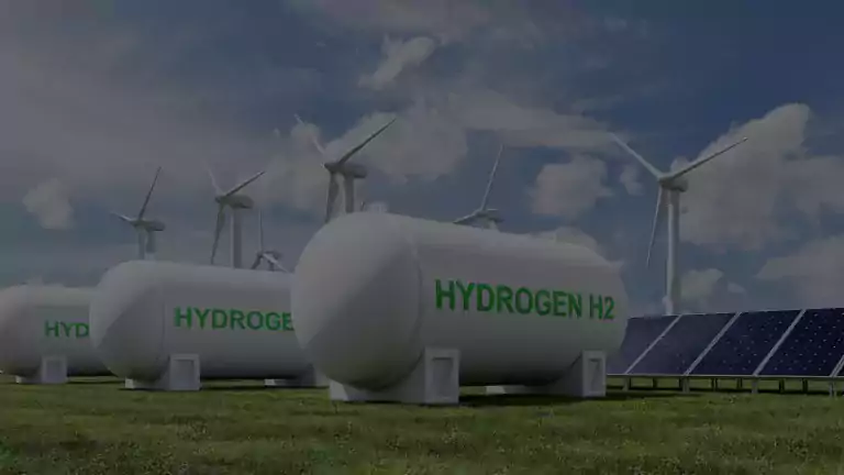 Large hydrogen storage tanks labeled 'Hydrogen H2' are placed on green grass, surrounded by wind turbines and solar panels under a blue sky with clouds, illustrating renewable energy production and storage.