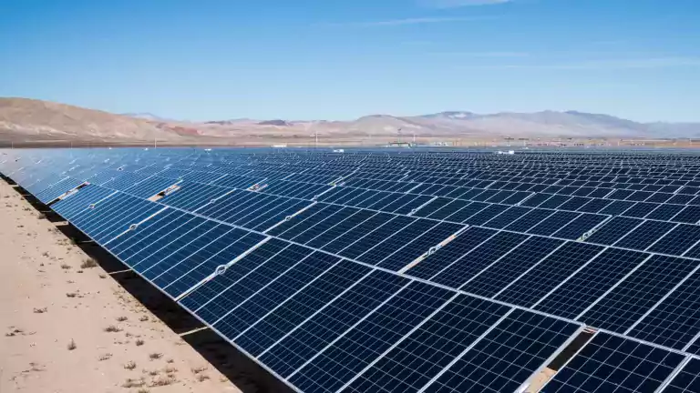 Large solar panel array in a desert landscape under a clear blue sky, with distant mountains in the background.
