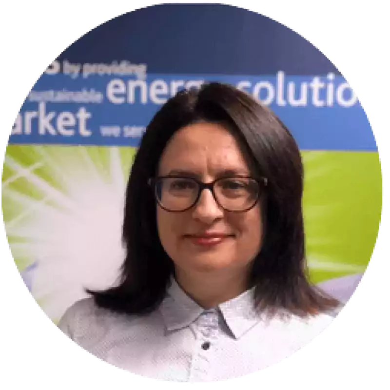Woman with straight dark hair and glasses wearing a white collared shirt, standing in front of a blue and green background with partially visible text about energy solutions.