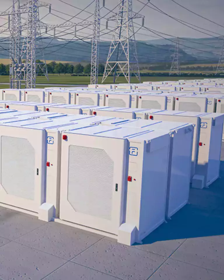 Rows of large white battery storage units are installed outdoors near high-voltage power lines and transmission towers, with green fields and hills in the background. The scene represents modern energy storage infrastructure for renewable energy or grid support.