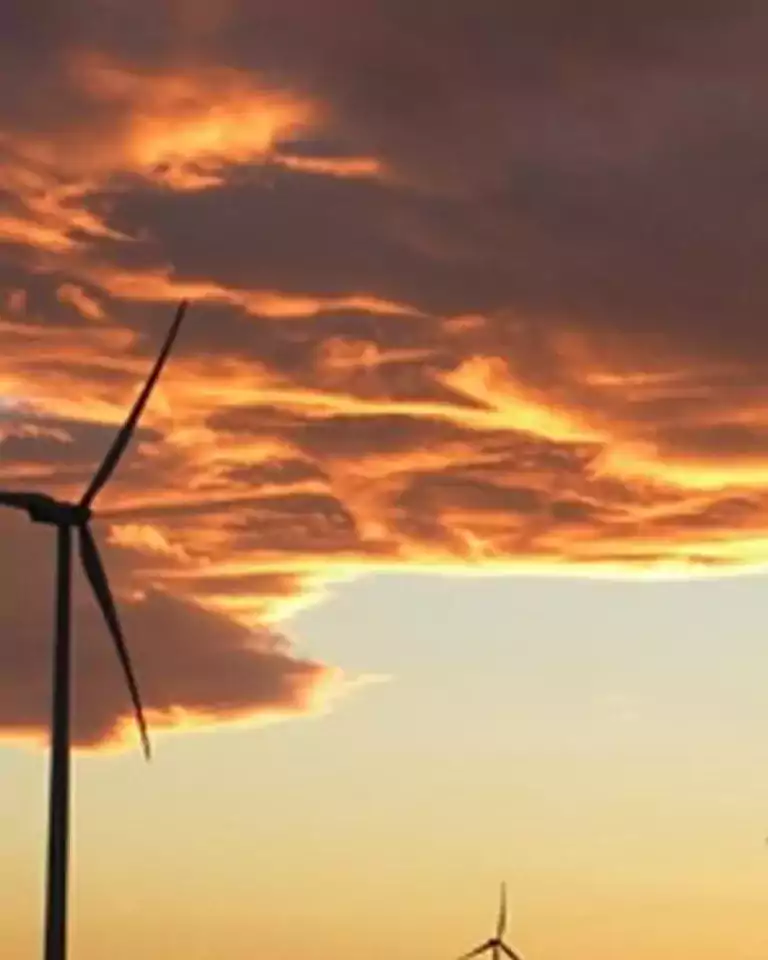 Wind turbines silhouetted against a dramatic sunset sky with orange and purple clouds, illustrating renewable energy in a natural landscape.