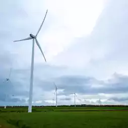 Several large wind turbines stand in a green field under a cloudy sky, generating renewable energy in a rural landscape.