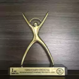 A gold-colored trophy shaped like a stylized human figure with outstretched arms and legs, standing on a black base with a plaque featuring Bulgarian text and a circular logo. The award is placed against a dark wooden background.