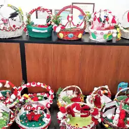 Colorful handmade baskets decorated with traditional Bulgarian Martenitsa ornaments, featuring red and white yarn dolls and flowers, displayed on and in front of a wooden cabinet in an office setting.