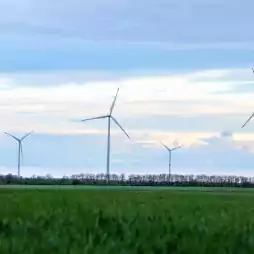 Several wind turbines stand in a green field under a partly cloudy sky at sunset, generating renewable energy in a rural landscape.
