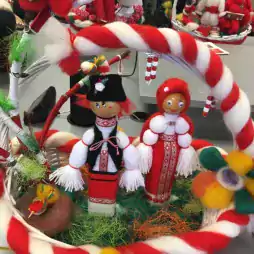 Handmade Bulgarian Martenitsa dolls dressed in traditional folk costumes placed inside a decorative basket with red and white yarn, green grass-like material, and colorful felt flowers, symbolizing the celebration of Baba Marta.