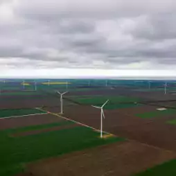 Aerial view of a wind farm with multiple wind turbines spread across green and brown agricultural fields under a cloudy sky.