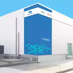 Modern white industrial building with a blue accent wall displaying the Fluence logo and partner company logos on the upper corner, set against a clear blue sky.